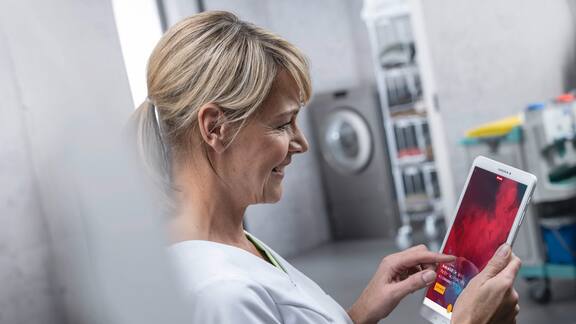 Eine Wäschereimitarbeiterin hält ein Tablet in der Hand, auf dem die Miele MOVE-Plattform zu sehen ist