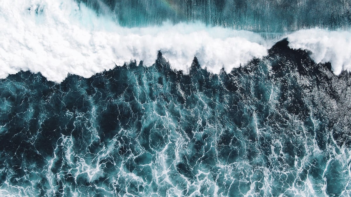 Luftaufnahme von Wellen, die auf das Meer treffen, mit weißer Gischt und tiefblauem Wasser.