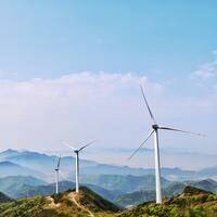 Drie windmolens staan op groene bergen onder een blauwe hemel