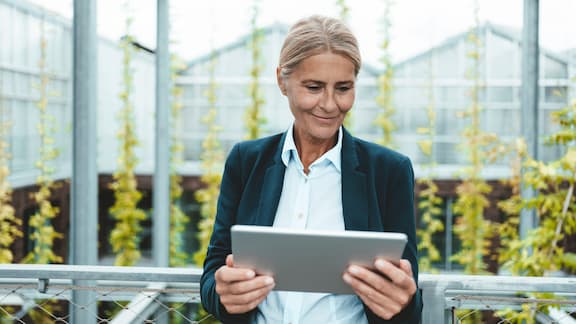 Mujer rubia en un invernadero con plantas, sosteniendo una tablet en sus manos