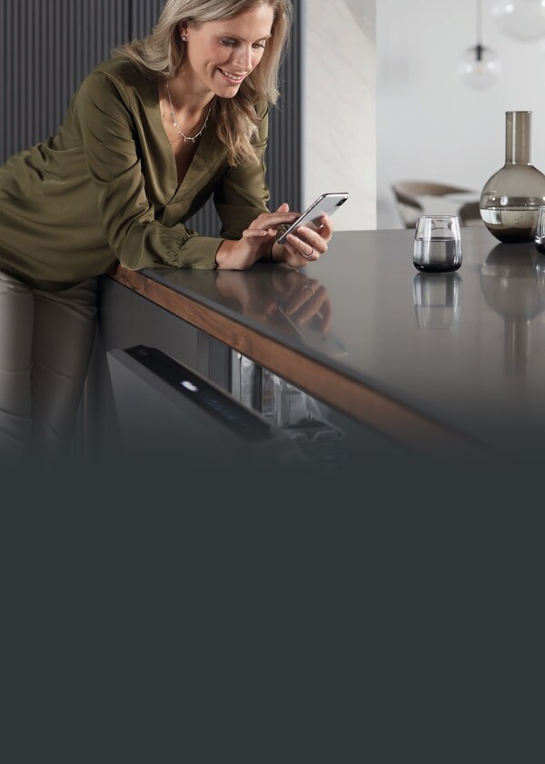 A woman looking at her phone while leaning on a kitchen bench