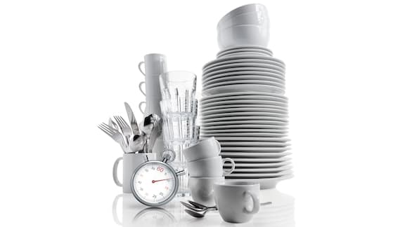 White dishes, cups and cutlery stacked next to a stopwatch