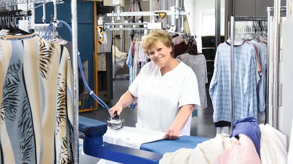 Eine Frau bügelt Kleidung in einem großem Wäschereiraum.