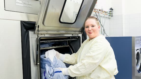 Eine Frau steckt schmutzige Wäsche in eine Trenndwandmaschine.