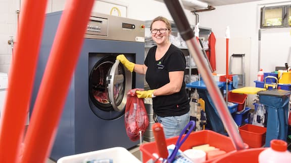 Eine Frau steckt schmutzige Wäsche in eine Miele Waschmaschine.