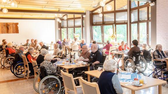 Viele Senioren sitzen in einem großen Raum gemeinsam an Tischen.