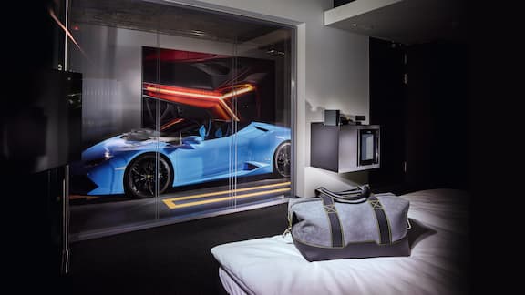 Vor dem Hotelzimmer des V8 Hotels steht ein blauer Sportwagen.