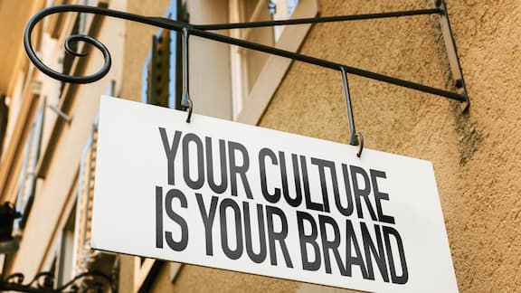 Ein Schild mit der Aufrschrift "Your culture is your Brand" hängt an einer Hauswand.
