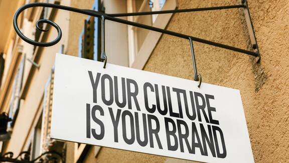 Ein Schild mit der Aufrschrift "Your culture is your Brand" hängt an einer Hauswand.