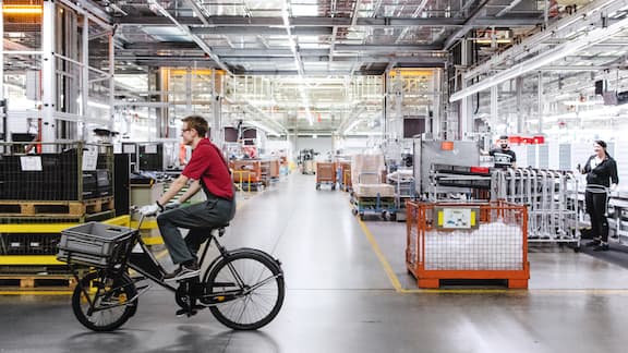 En Miele-produktionsanläggning sedd inifrån, en medarbetare kör genom bilden med sin cykel
