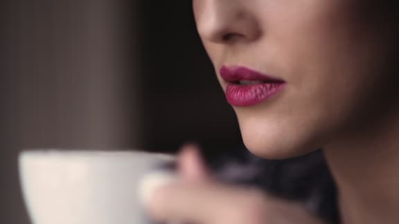 Kobieta z czerwoną szminką na ustach trzymająca w ręku filiżankę kawy