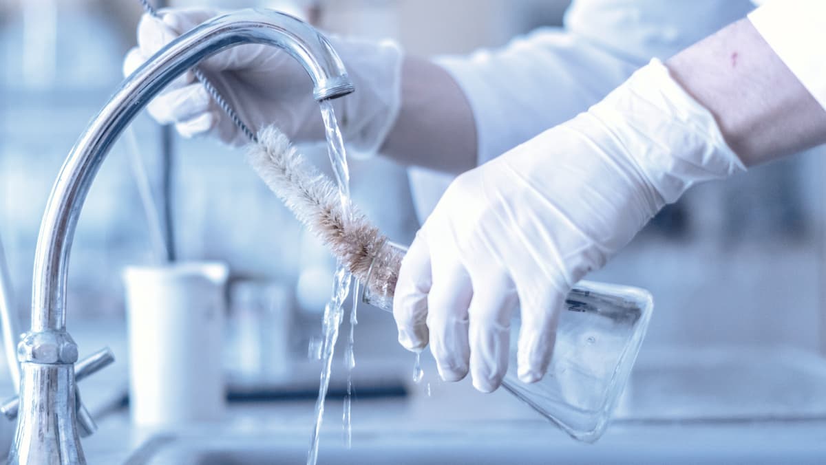 Un assistente di laboratorio lava un'ampolla di vetro a mano