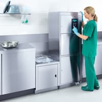 Zdravotní sestra tiskne tlačítko nabídky na nerezovém mycím a dezinfekčním automatu podložních mís v přípravní lince.