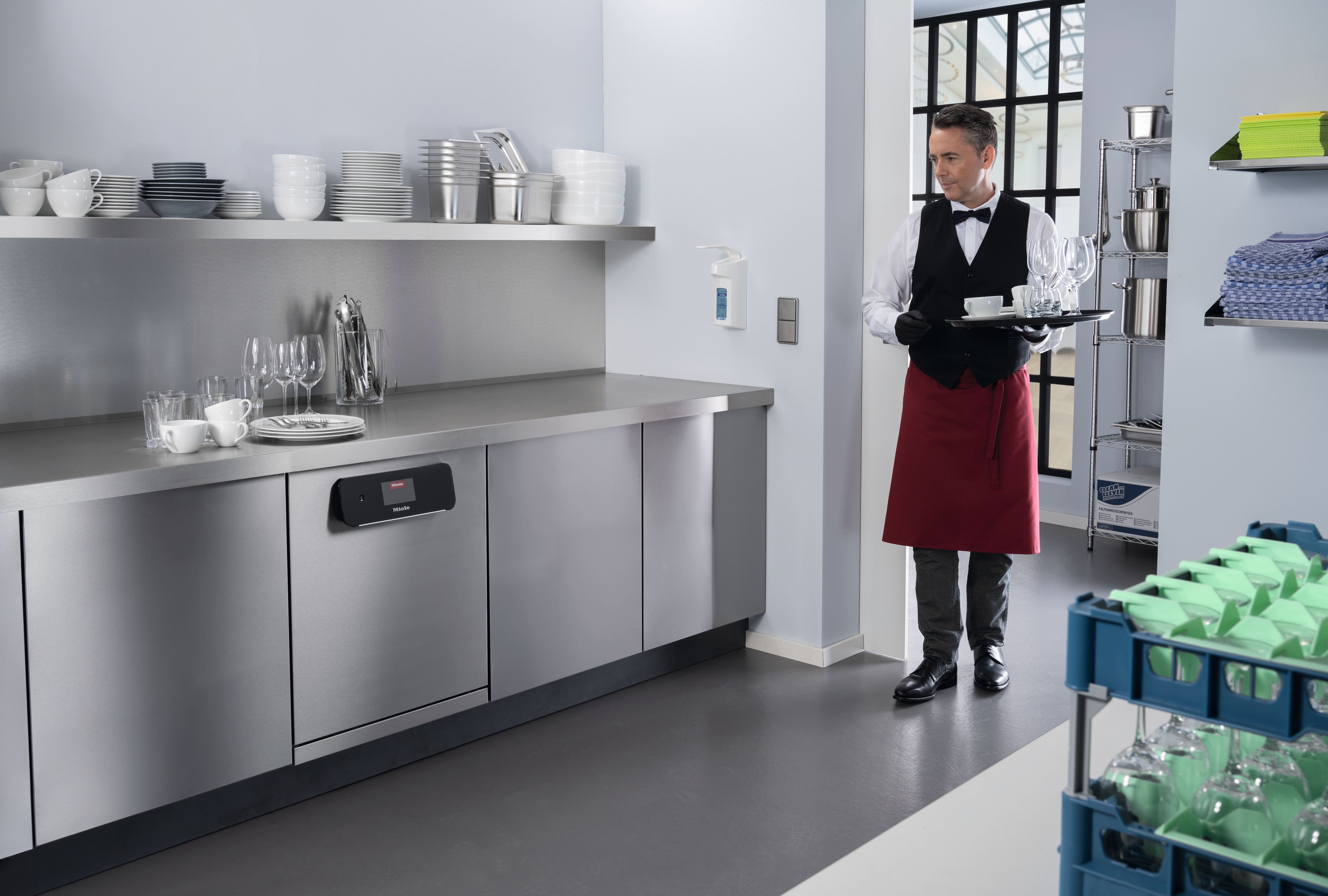 Image of a waiter bringing used crockery into a kitchen where a Miele dishwasher stands