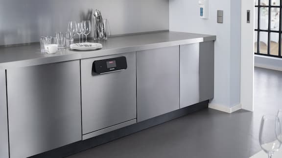 Bancada de cozinha clara com máquinas de lavar louça MasterLine da Miele Professional e louça 