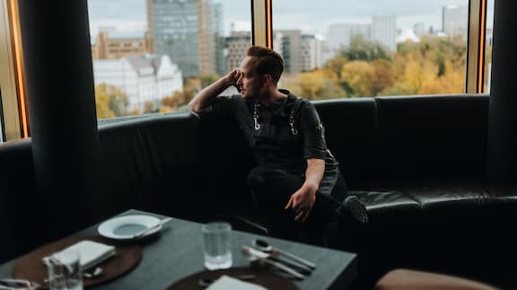 Chef-de-cuisine Jonas Zörner sits on a couch, looking out of the restaurant window.
