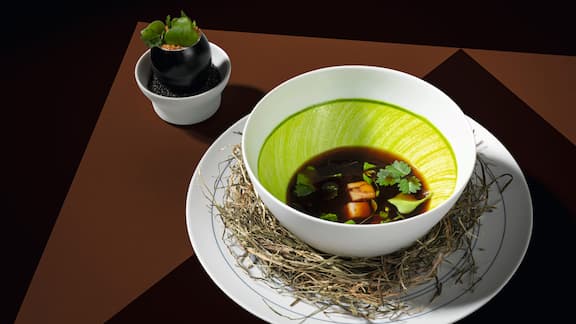 A white porcelain dish with a light green in the centre, filled with soup.