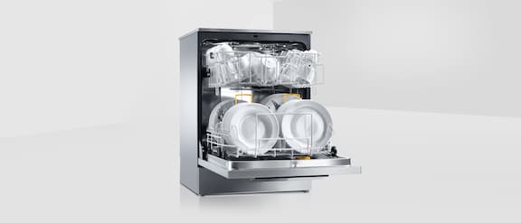 Range of Miele Professional Tank dishwasher: One throughput dishwasher and three tank dishwasher in a row, opened door equipped with baskets, glass and cutlery on grey background. In front another tank dishwasher with opened door and equipped.