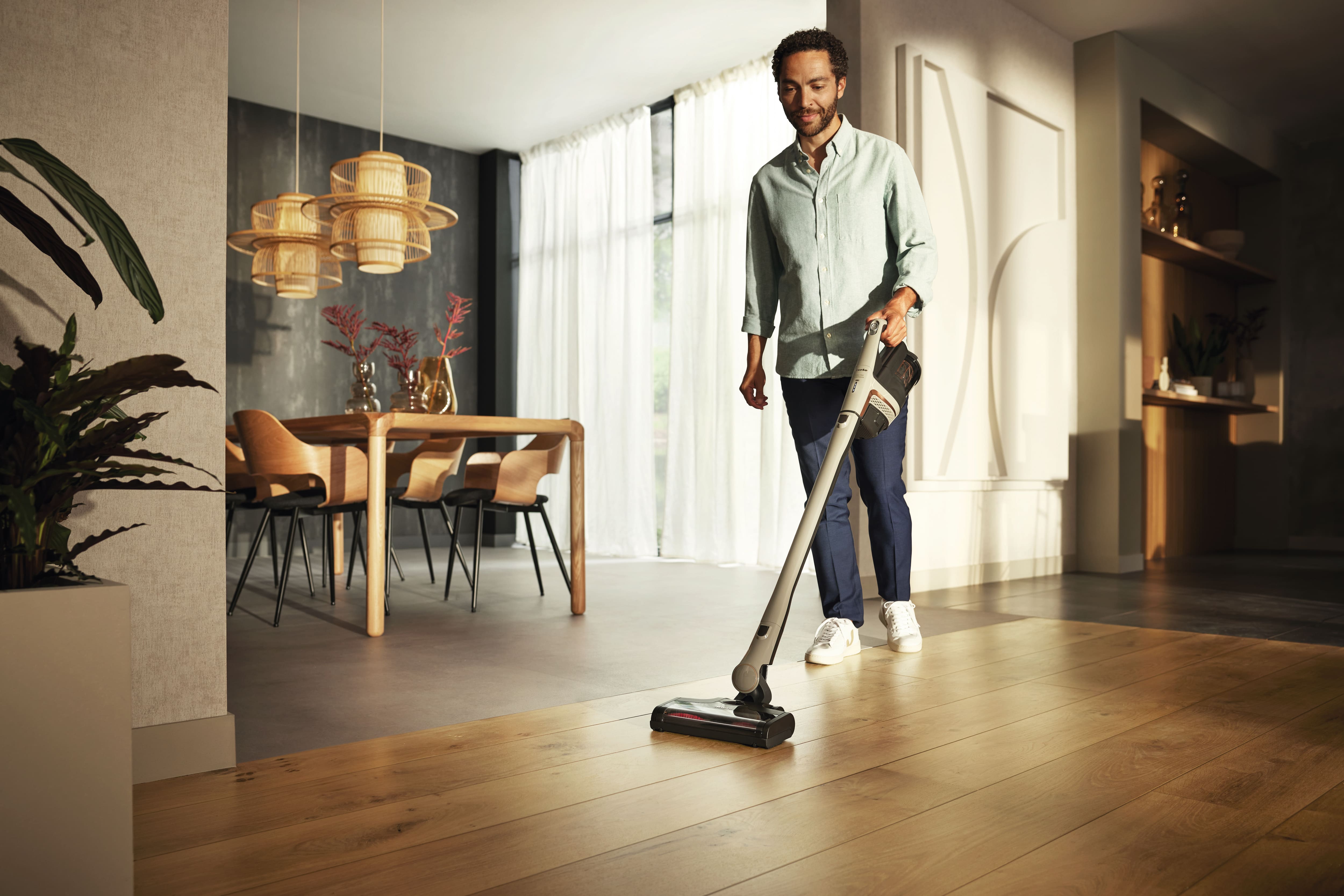 Man in living area cleaning with a cordless stick vacuum cleaner