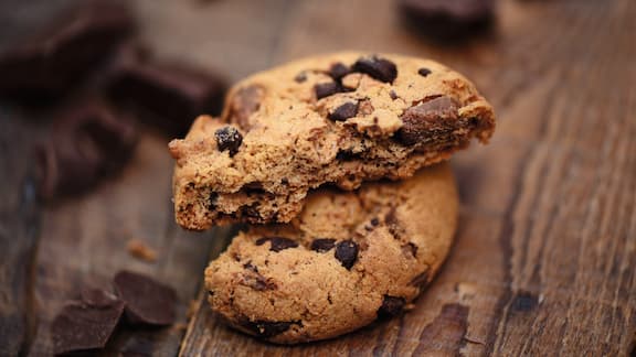 A cookie, broken into two pieces, lying on dark wood.  