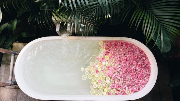 A bird's-eye view of a bathtub, filled with water, blossoms and lemon slices.