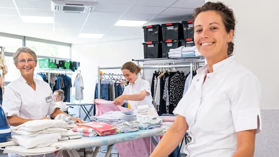 Three employees from the retirement home stand in the laundry and smile for the camera