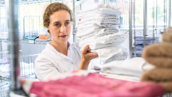 A colleague places folded towels on a rack in the laundry