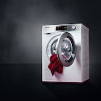 The Miele SmartBiz washing machine is displayed on a black backgrund. The door is opened with a red red towel hanging out of the drum.