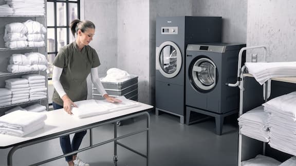 Una donna in una lavanderia con macchine Miele piega gli asciugamani