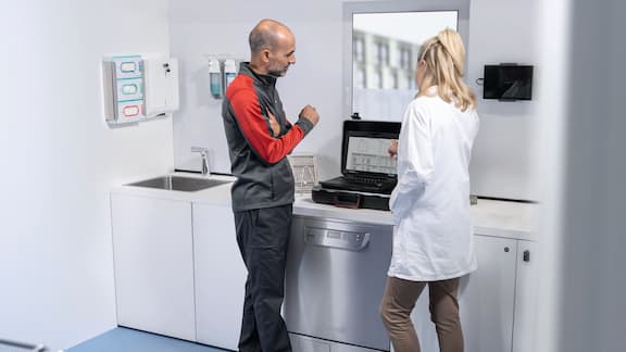 Un technicien de service vérifie un stérilisateur compact en présence d’une assistante médicale.