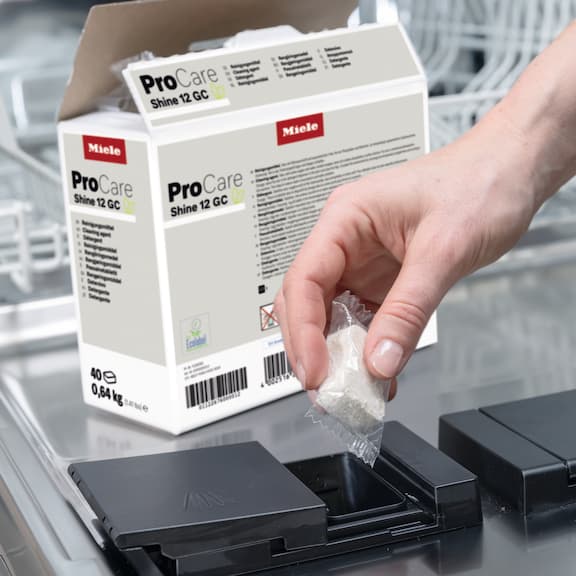 A person is placing a ProCare Shine Tab into the dispensing chamber of a freshwater dishwasher.