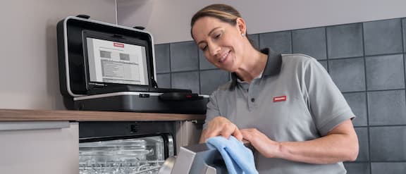 En servicetekniker tørker av en oppvaskmaskin i rustfritt stål med en mikrofiberklut