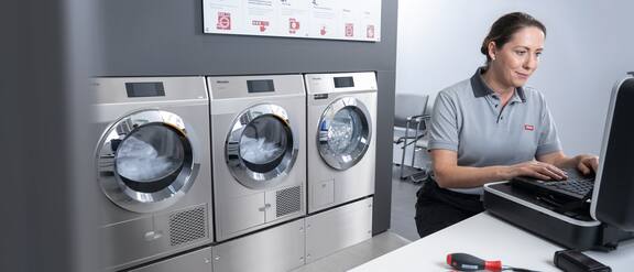 En servicetekniker legger inn data på den bærbare datamaskinen sin – et vaskeri kan sees i bakgrunnen