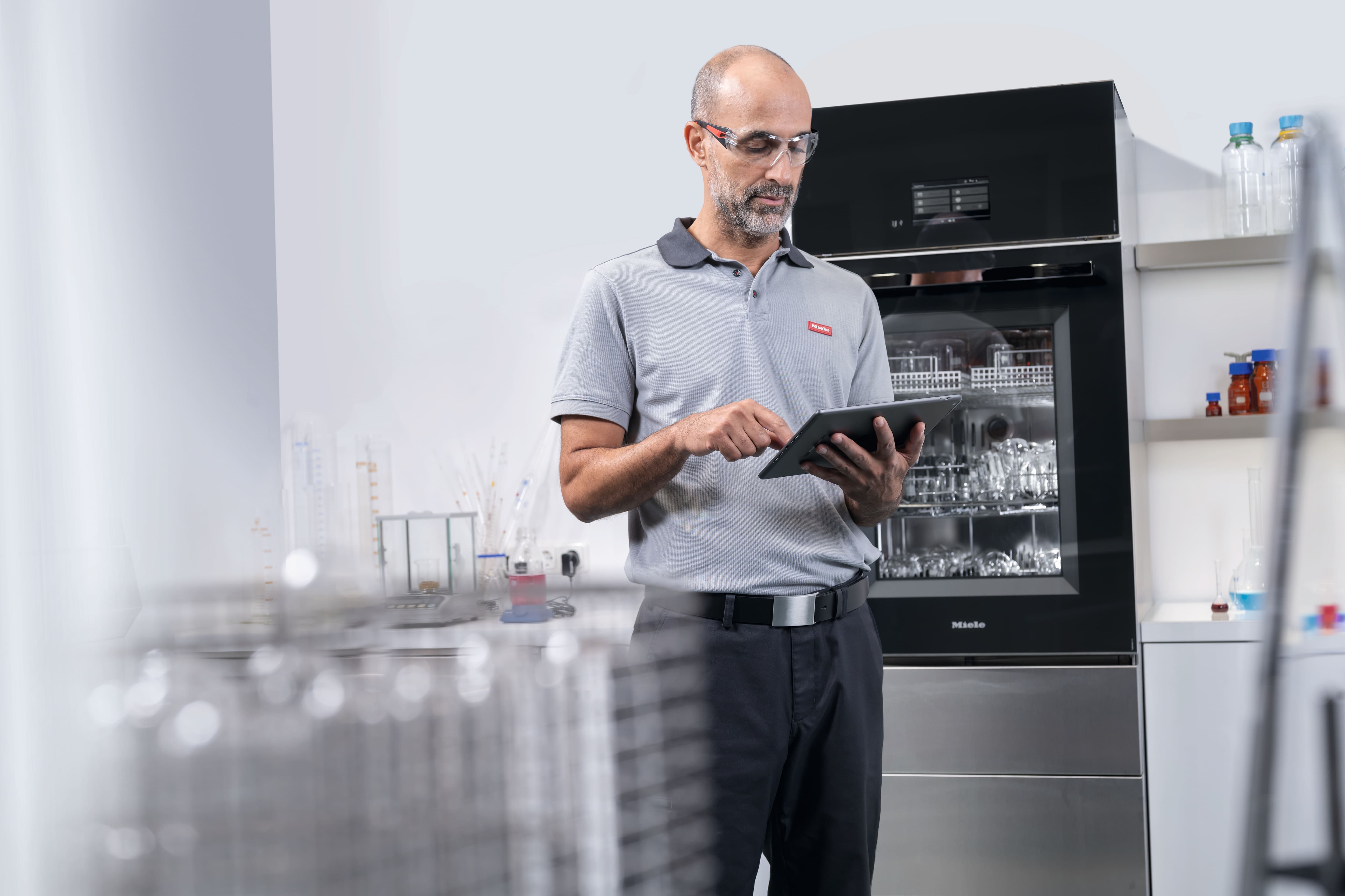 Ein Servicetechniker steht vor einem SlimLine Laborspüler mit einem Tablet in der Hand.
