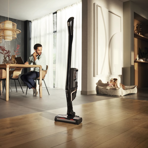 Standing Miele vacuum with dog laying in a dog bed behind it