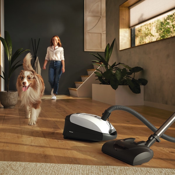 White Miele canister vacuum with a dog and woman behind it