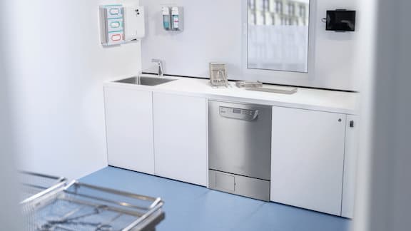 A medical assistant pictured tidying up the reprocessing room at the practice. In the foreground, there is a container for the ProCare Med process chemicals.