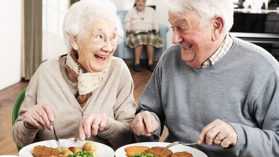 Un couple de personnes âgées est assis à une table et déjeune dans une maison de retraite