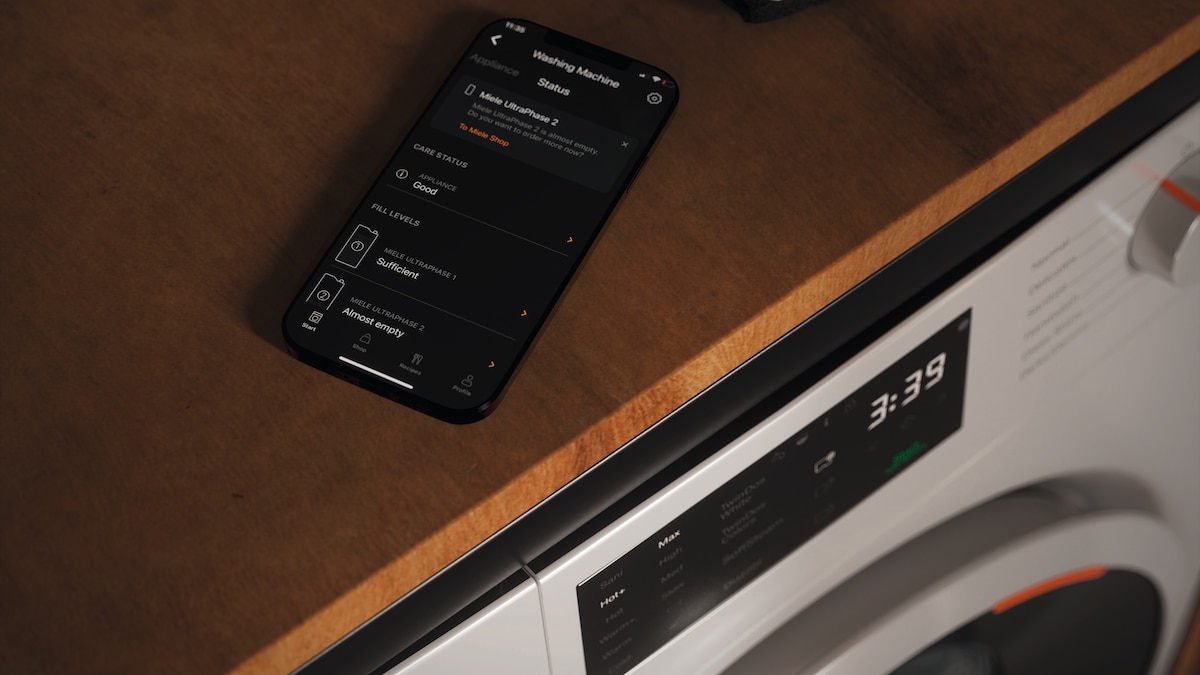 phone with Miele app open on the consumption dashboard on top of a Miele washing machine