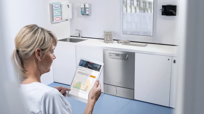 Työntekijä tabletin kanssa välinehuoltotilassa tarkistamassa ohjelman kulkua Miele MOVE MedDent+ -ohjelmiston avulla.
