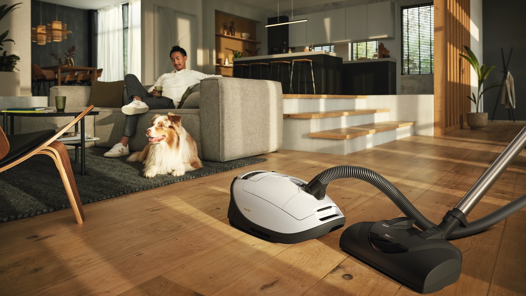 Image of a parked vacuum cleaner and a man on a couch next to a dog
