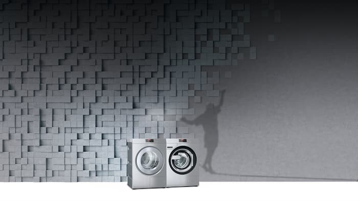 Benchmark Performance Plus Trockner und Waschmaschine stehen vor einem grauen Hintergrund. Daneben ist ein schwarzer Schatten von einem Slackliner zu sehen.