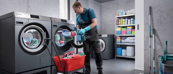Picture from a laundry where a man is loading a Miele washing machine.