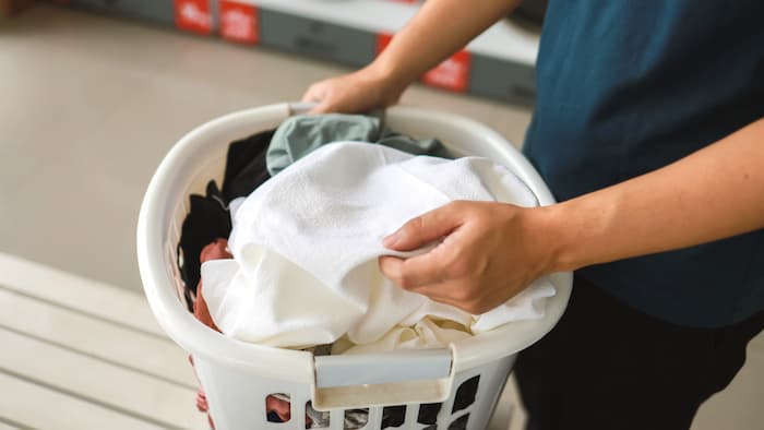 A woman is carrying a laundry basket and filling a washing machine in the launderette with laundry. 