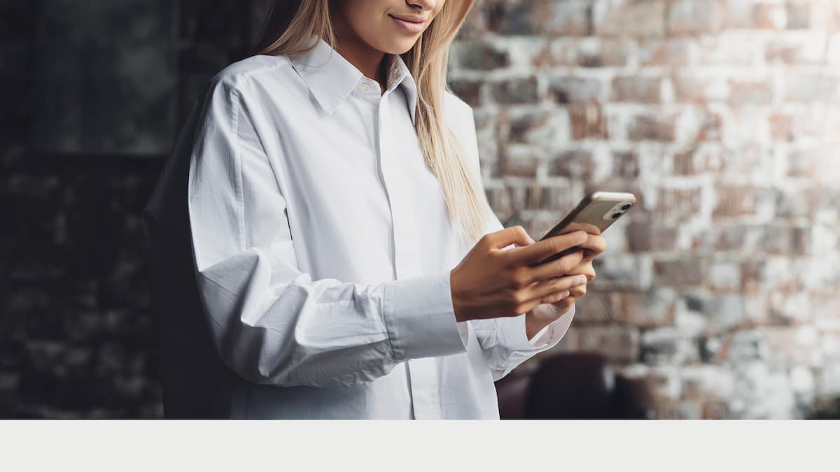 Eine junge Frau hält ein Smartphone in ihrer Hand und bedient es. Die Hand befindet sich in der Mitte des Fotos.