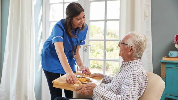 Eine Pflegekraft bringt einem Bewohner das Essen auf einem Tablett ins Zimmer
