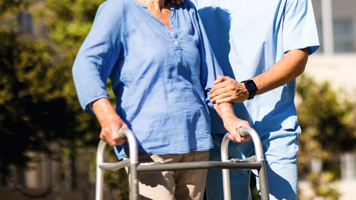 A male carer accompanies an old lady on a walk in the fresh air 