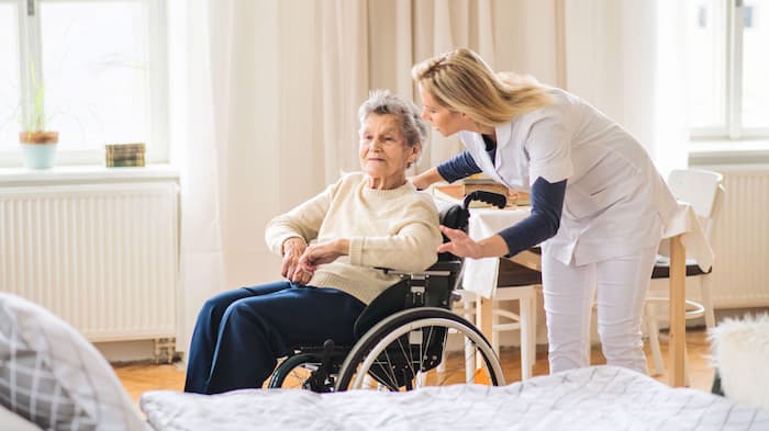Nurse leaning towards elderly patient on wheel chair in care home bedroom