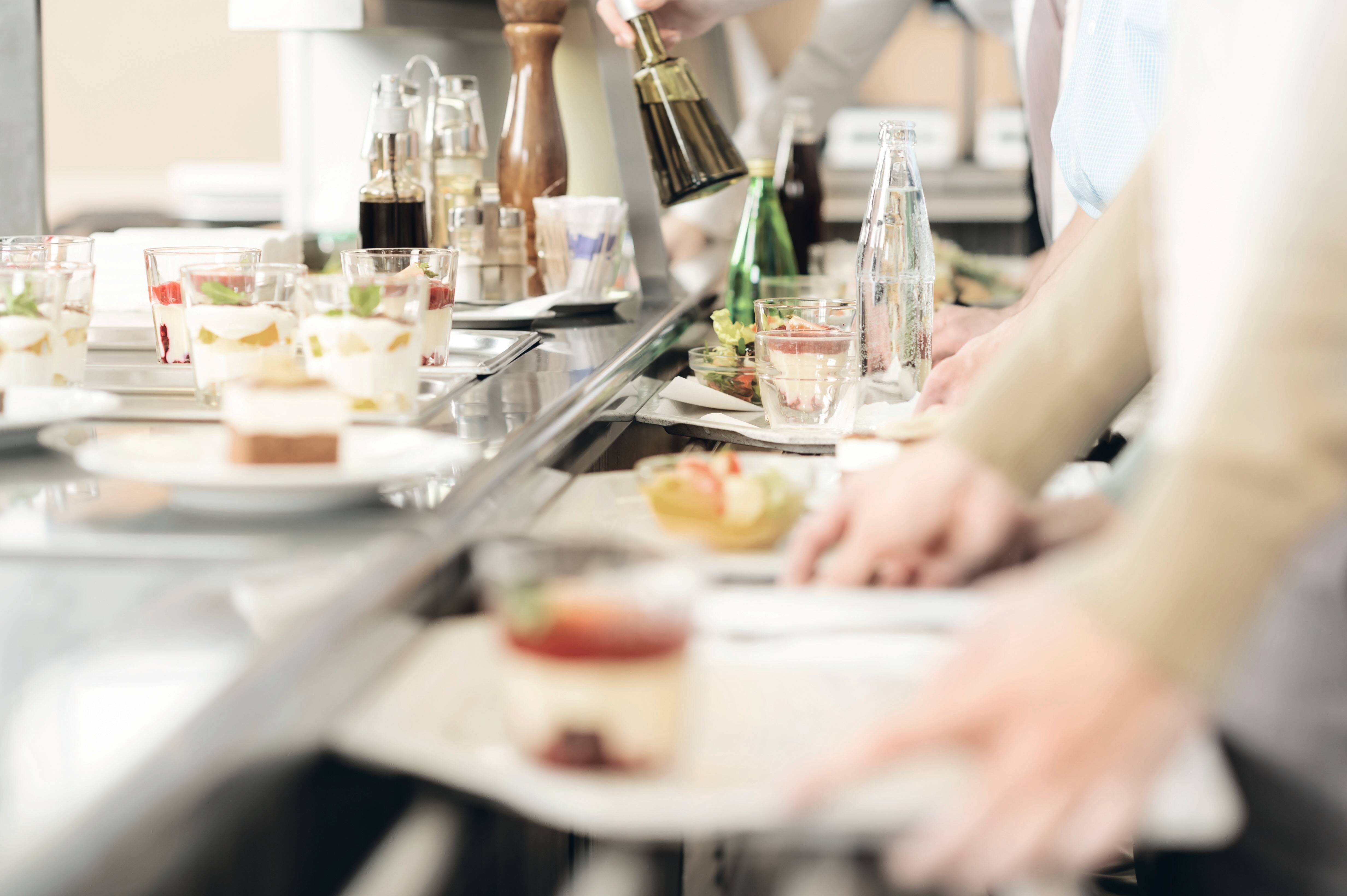 Picture of a queue of people waiting in a canteen with trays and crockery