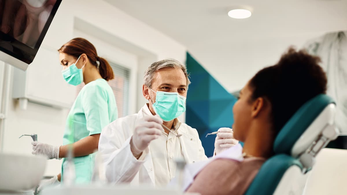 Dentysta w masce przygotowuje się do zabiegu na pacjencie siedzącym na fotelu dentystycznym